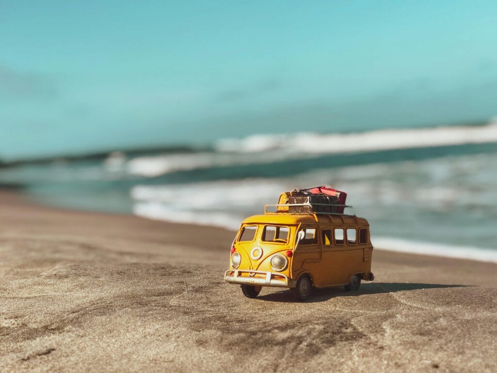 Vakantie busje strand reisverzekering Klein busje op het strand met bagage als symbool voor reizen en een reisverzekering